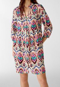 Vestido impreso multicolor que presenta un escote con cuello, mangas tres cuartos y cintura elastizada. El patrón incluye formas verdes, rosas y azules.