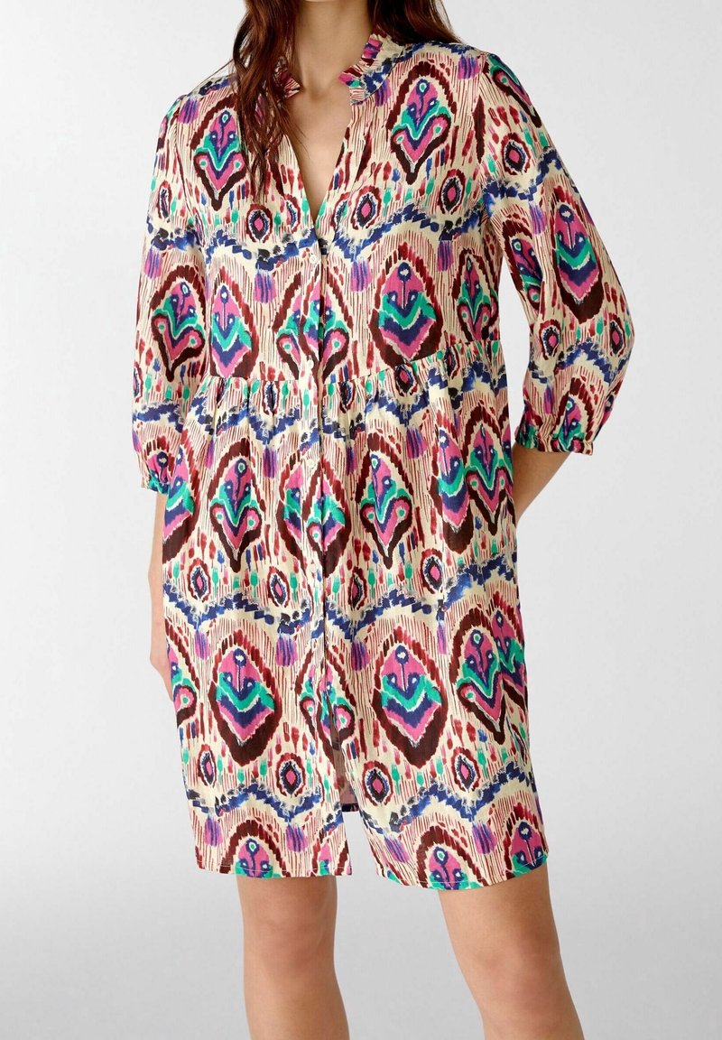 Vestido impreso multicolor que presenta un escote con cuello, mangas tres cuartos y cintura elastizada. El patrón incluye formas verdes, rosas y azules.