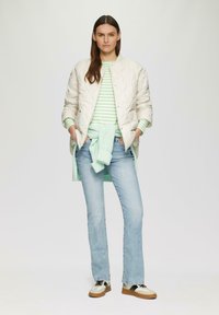 Veste bomber beige matelassée sur un top rayé vert et blanc, associée à un jean évasé bleu clair et des sneakers à bloc de couleurs.