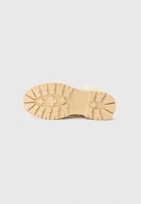 Semelle d'une botte avec un design texturé et robuste, dotée de crampons distincts, sur un fond clair et uni.