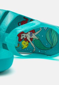 Akvatransparent sandal med glitter, med et tegneserie-design av en havfrue og fisk på sålen. Justerbare stropper for passform.
