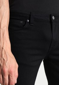 Černé džíny z denimu s úzkým střihem, standardním zapínáním na knoflík a zip, bočními kapsami a jemnými detaily švů.