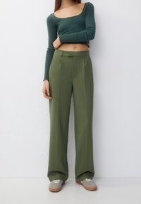 Green ribbed long-sleeve top paired with high-waisted, olive green wide-leg trousers. The outfit is completed with grey sneakers and a simple design.