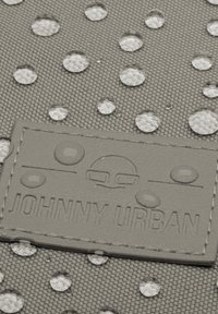 Szürke szövettáska vízálló vízcseppekkel és texturált felülettel, amelyen egy szürke dombornyomott címke olvasható: "JOHNNY URBAN."