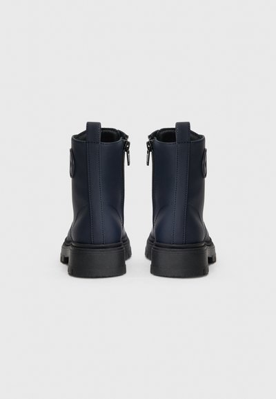 Anfibi navy in materiale sintetico liscio, con cerniere laterali, linguette rotonde e suole in gomma nera con un motivo di battistrada testurizzato.