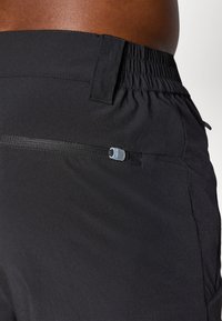 Schwarze Sportshorts mit elastischem Bund, ausgestattet mit einer Reißverschlusstasche und einer glatten Textur, entworfen für Komfort und Funktionalität.