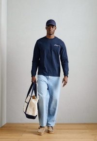 Tumesinine pikkade varrukatega särk, helesinised laiad teksad ja beežid kingad. Hoides beeži kangast kotti tumehallide aktsentidega.