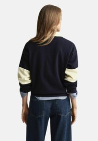 Marineblauwe sweatshirt met crème-kleurige mouwen, geribbelde manchetten en een ronde halsontwerp. Gedragen over een gestreept shirt en gecombineerd met donkere denim.