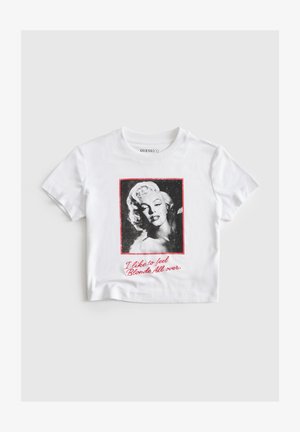Witte T-shirt met korte mouwen met een zwart-wit portret van een blonde vrouw en rode tekst met de tekst "Ik hou ervan om me overal blond te voelen."
