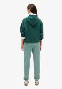Sudadera extragrande de color verde oscuro con capucha, combinada con pantalones jogger de color verde claro. Ambas prendas están hechas de tela suave con puños elásticos.