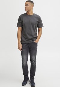 Camiseta de manga corta en color carbón combinada con jeans negros desgastados y zapatillas deportivas oscuras, con cuello redondo y corte relajado.