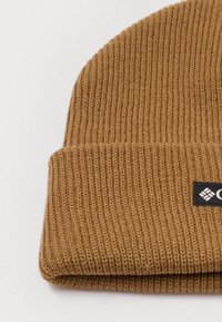 Gorro de malha castanho com textura canelada. Apresenta uma dobra na bainha e um pequeno patch de logo preto na lateral. Material suave com uma aparência quente.