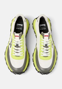 White and gray sneakers with a thick black sole, neon yellow accents, and reflective details; features a lace-up design and GORE-TEX branding.