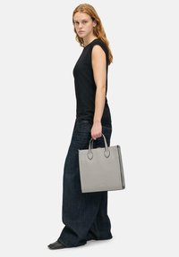 Szara skórzana torba typu tote z dwoma zaokrąglonymi uchwytami, prostokątny kształt, gładka tekstura, minimalistyczny design i subtelne logo.