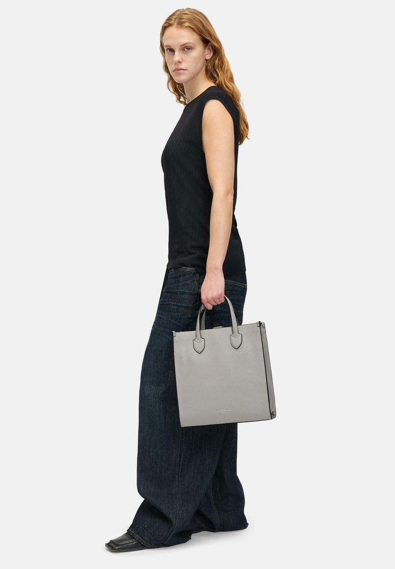 Szara skórzana torba typu tote z dwoma zaokrąglonymi uchwytami, prostokątny kształt, gładka tekstura, minimalistyczny design i subtelne logo.