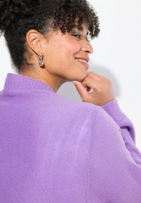 Maglione viola lavorato a maglia con colletto alto e polsini a coste. Presenta un motivo testurizzato e una vestibilità rilassata, arricchito da orecchini a goccia in argento.