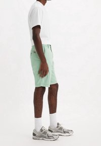 Miętowe szorty o prostym kroju, z bawełnianej tkaniny, z kieszeniami po bokach i z tyłu oraz metką z tyłu. W zestawie z białą koszulką i szarymi tenisówkami.