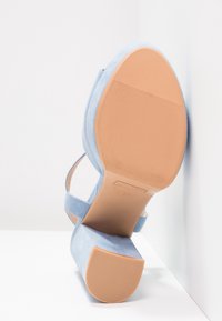 Sandale à talon bloc en daim bleu clair vue depuis la semelle sur fond blanc dans un angle.