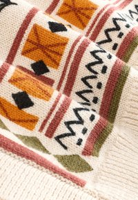 Strikket stof i creme med mønstrede accenter i orange, sort og grøn. Indeholder geometriske motiver og teksturerede striber.