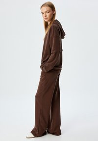 Bruine hoodie met een ontspannen fit, oversized silhouet en zijzakken, gecombineerd met bijpassende wide-leg broek, zachte textuur en een minimaal ontwerp.