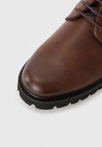 Brun læder sko med en glat finish, rund tå og kontrasterende sort gummisål med teksturerede detaljer og en syet kant.