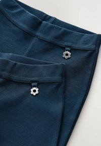 Marineblaue Hosen aus weichem Stoff, mit einem glatten Bund und zwei silbernen, blumenförmigen Akzenten auf der Vorderseite.