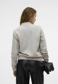 Ljust grå bomberjacka med en texturerad yta och ribbad nederkant, kombinerad med svarta byxor i konstläder med krokodiltryck och en svart kuvertväska.