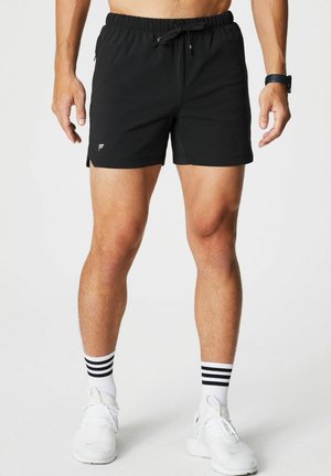 Schwarze Badeshorts mit elastischem Bund und Kordelzug. Mit Seitentaschen und kleinem Logo. Getragen mit weißen Turnschuhen und gestreiften Socken.