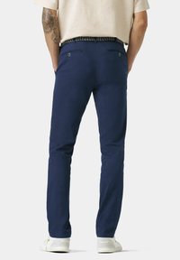 Navyblauwe chino's van katoen, met een slim fit, twee achterzakken en een geweven riem. Witte sneakers maken de outfit compleet.