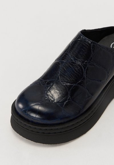 Sandalie din piele marine, slip-on, cu un model texturat și crăpat, talpă neagră din platformă și vârf rotunjit. Design minimalist, fără elemente de prindere vizibile.