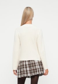 Pull en crème à côtes avec des manches longues, associé à une jupe évasée en plaid marron. La texture douce et le col rond sont des détails remarquables.