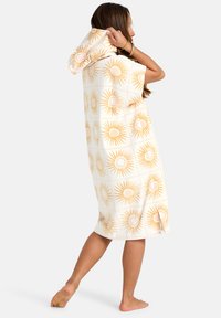 Toalla con capucha que presenta una base blanca con un patrón de destellos dorados. La tela parece suave y absorbente, con un diseño relajado hasta la rodilla.