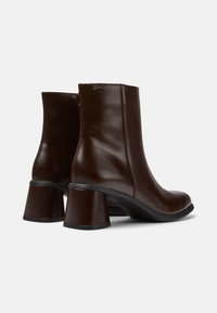 Paire de bottines en cuir brun foncé avec talons blocs et fermetures éclair latérales, vues de dos sur un fond blanc uni.