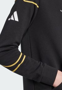 Felpa nera con tessuto testurizzato. Caratterizzata da audaci strisce gialle sulle maniche e un accento di logo bianco sulla parte superiore del braccio.