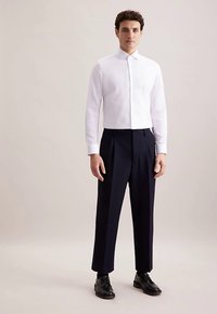 Witte blouse met kraag, gecombineerd met donkere, op maat gemaakte broek. De blouse heeft een aansluitend ontwerp, terwijl de broek een geplooide voorkant heeft. Zwarte schoenen maken de look compleet.