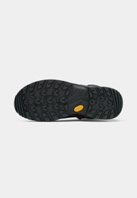 Schwarze Gummisohle mit aggressivem Profil, ausgestattet mit einem gelben Vibram-Logo und strukturierten Akzenten für besseren Halt.