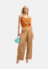 Bruine wijde broek met een zijstrik, gecombineerd met een oranje mouwloos topje, turquoise kra necklace, en een kleine turkooise handtas.