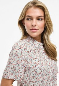 Lekka, krótka bluzka z krótkim rękawem w kwiatowy wzór w odcieniach czerwieni, niebieskiego i kremowego. Posiada kołnierzyk oraz zapięcie na guziki z przodu. Miękka w dotyku.