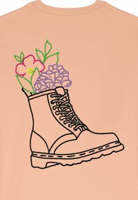 Vyšívaná černá bota na broskvovém pozadí, s barevnými květinami a zelenými listy vystupujícími z vrchu.