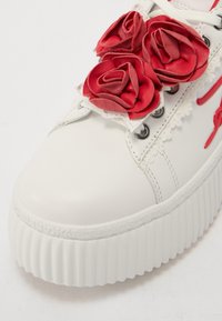 Bílý sneaker s platformovou podrážkou, ozdobený třemi látkovými červenými růžemi, krajkovým detailem a černými očky pro tkaničky.