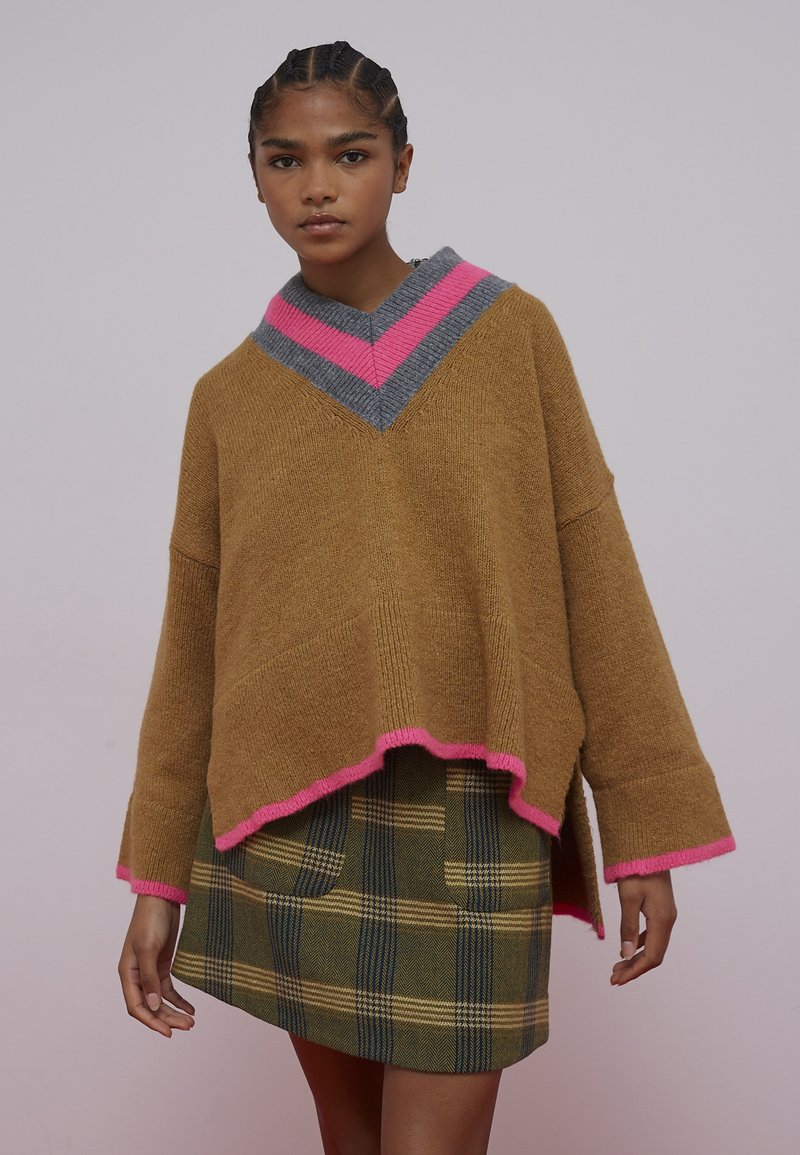 Rjavo pleten pulover velike velikosti z rožnato-sivim ovratnikom v obliki chevron, kombiniran z zeleno karo krilom z našitimi žepi.