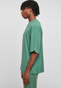 Tricou verde oversized cu mânecă scurtă, realizat dintr-un material moale, având un decolteu rotund și o siluetă lejeră. Poala are un detaliu mic cu logo.
