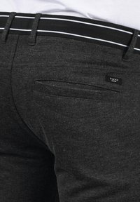 Pantalones de mezclilla negros con una superficie texturizada, que presentan un ajuste slim, una cinturilla negra con rayas blancas y una pequeña etiqueta en el bolsillo.