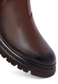 Stivale alla caviglia in pelle marrone con texture liscia, dotato di una robusta suola in gomma nera con un motivo ruvido e dettagli di cucitura sottili.