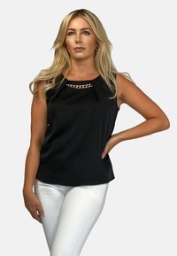 Czarna bezrękawnik z łańcuszkiem w dekolcie, o gładkiej fakturze i luźnym kroju, w połączeniu z białymi spodniami.