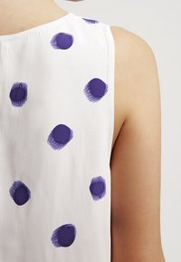 Top senza maniche in tessuto leggero con macchie di pennellate viola sparse. Il retro presenta una finitura liscia e dettagli di cucitura sottili.