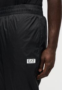 Μαύρο παντελόνι φόρμας από ελαφρύ ύφασμα με σχέδιο σε πλέγμα. Διαθέτει ελαστική μέση και μια ταμπέλα με λογότυπο ραμμένη στο πλάι.