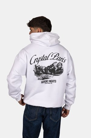 Un hoodie blanc avec une grande impression graphique noire au dos représentant un paysage montagneux, avec le texte "Crystal Paris Nordic Nights."