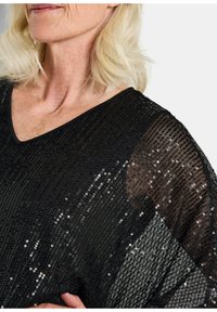 Schwarzes Paillettenoberteil mit V-Ausschnitt, in einem leichten, transparenten Design; Pailletten in vertikalen Linien angeordnet, die Textur und Glanz erzeugen.