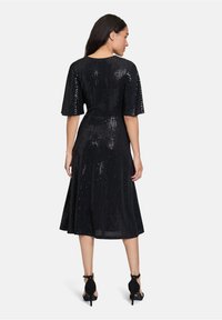 Robe en sequins noirs avec des manches courtes, une longueur mi-mollet, une taille cintrée et une jupe évasée. Elle présente une texture brillante et un motif subtil.